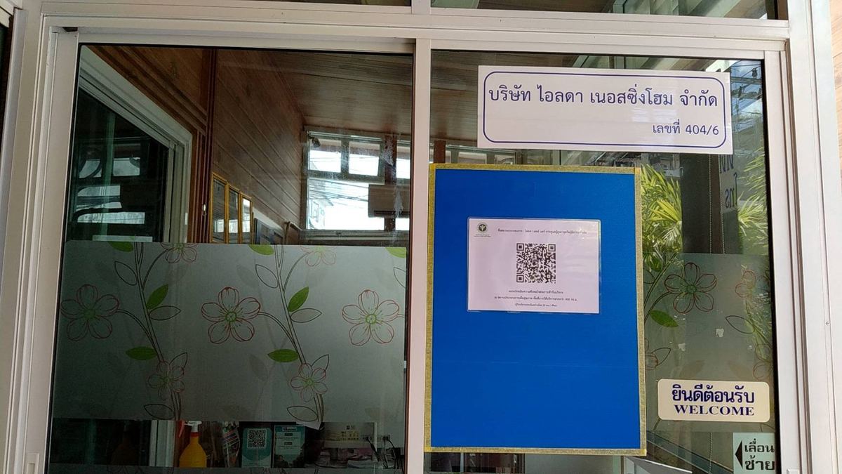 ประตูกระจกทางเข้าบริษัท ไอลดา เนอสซิ่งโฮม จำกัด มีป้ายชื่อบริษัทและป้ายยินดีต้อนรับ