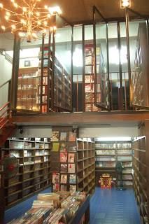 ภายในร้าน Armchairbooks มีชั้นหนังสือเรียงสูงทั้งชั้นล่างและชั้นบน พร้อมโคมไฟระย้า