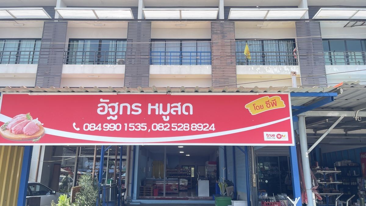 หน้าร้านอัฐกร หมูสด ป้ายชื่อร้านสีแดงบนอาคารพาณิชย์ มองเห็นตู้แช่และชั้นสินค้าภายในร้าน