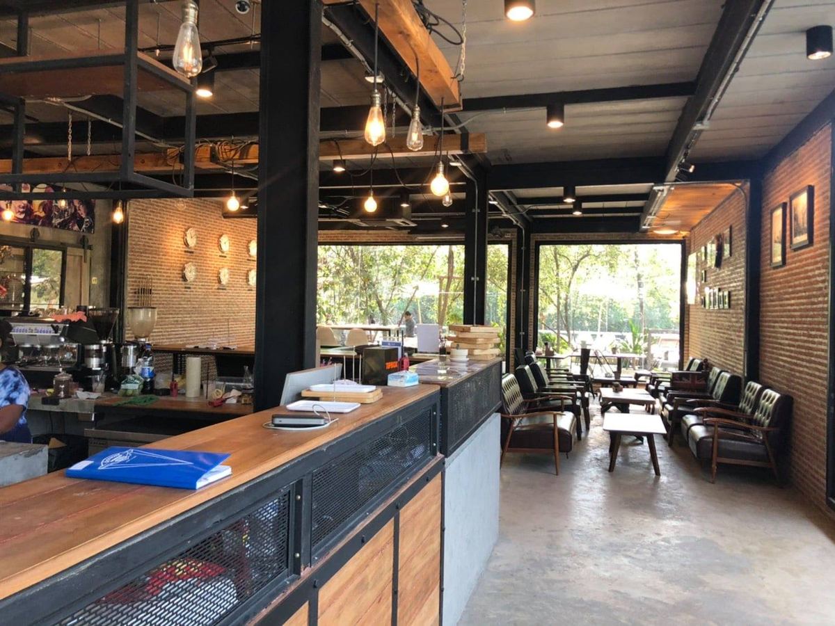 ภายในบ้านYAIเวียง มีเคาน์เตอร์ไม้ยาว ผนังอิฐ และมุมโซฟาเปิดโล่งมองเห็นต้นไม้