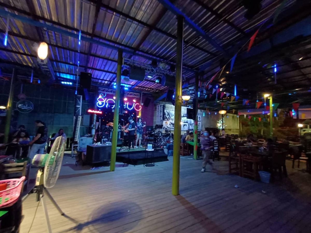 ร้านฮัก (Hug) ยามค่ำ ลานโต๊ะไม้ เวทีดนตรีสด และป้ายไฟนีออนชื่อร้าน