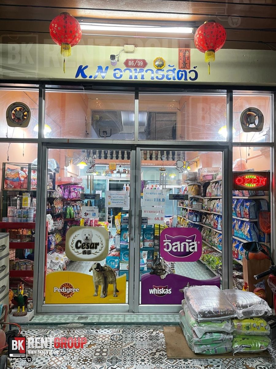 หน้าร้าน K.N. อาหารสัตว์ ป้ายชื่อสีน้ำเงิน โคมแดงสองดวง ประตูกระจกติดสติกเกอร์อาหารสุนัขและแมว