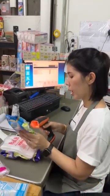 ที่จุดขายร้านครูยุ้ย แพ็คเกจจิ้ง มีการยิงบาร์โค้ดสินค้าด้วยเครื่องสแกนแบบถือ หน้าจอขายเปิดอยู่ด้านหลัง