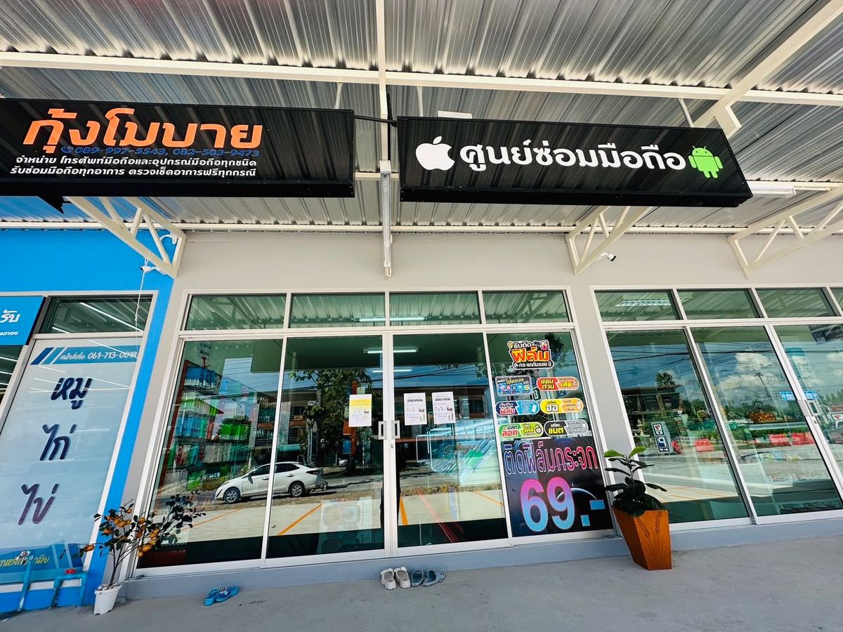 หน้าร้านกุ้งโมบาย ป้ายชื่อร้านสีส้มบนพื้นดำ ข้างป้ายศูนย์ซ่อมมือถือ และประตูกระจกหน้าร้าน