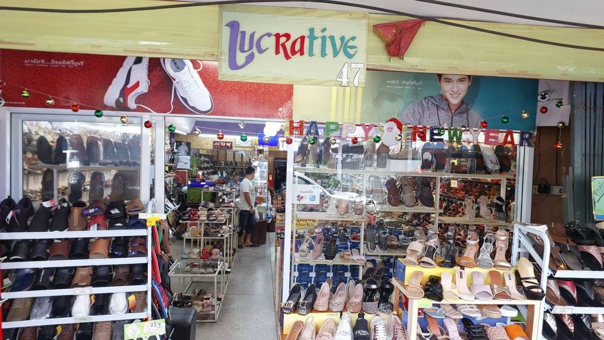 หน้าร้าน Lucrative ป้ายชื่อร้านตัวอักษรหลากสี มีชั้นวางรองเท้าผู้หญิงและรองเท้าแตะหน้าร้าน