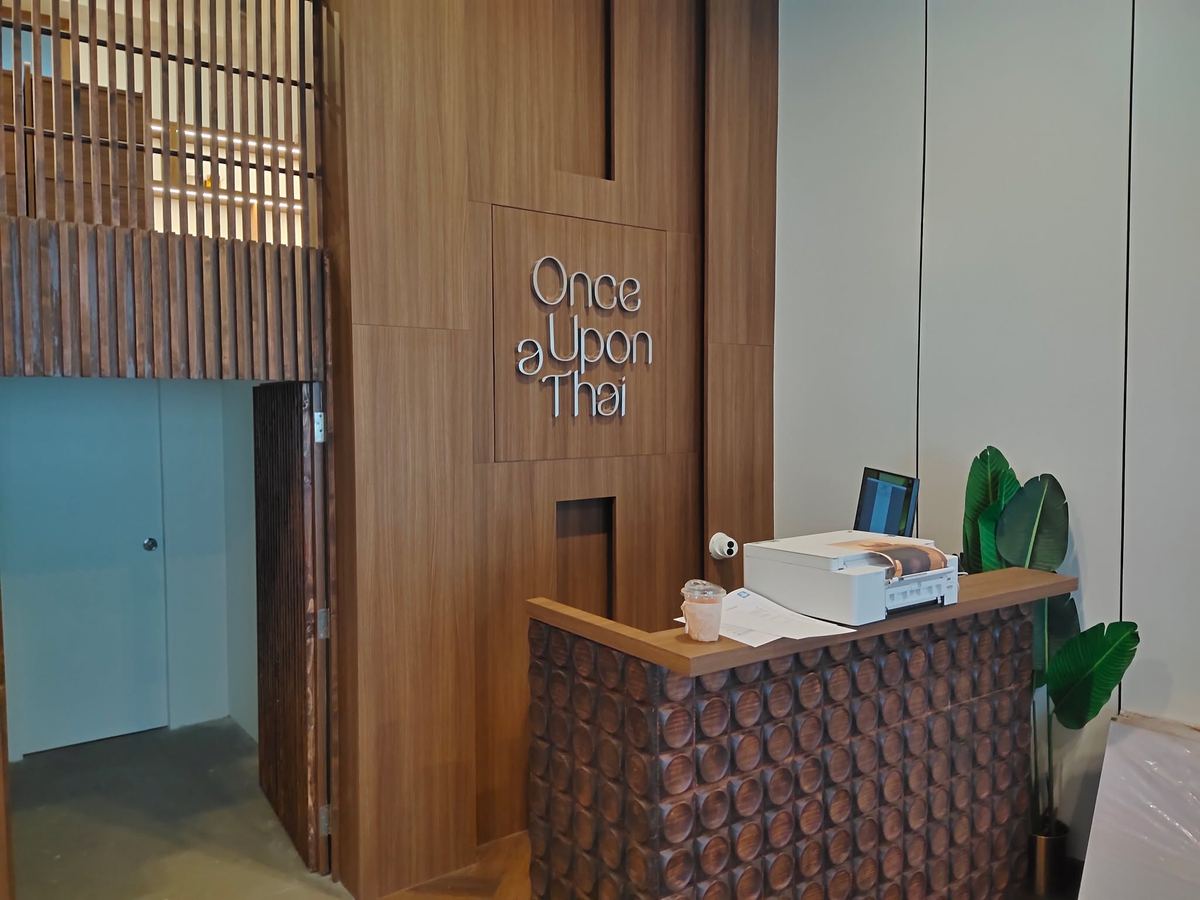 เคาน์เตอร์ต้อนรับของ Once Upon a Thai หน้าผนังลายไม้ที่ติดโลโก้ชื่อร้าน