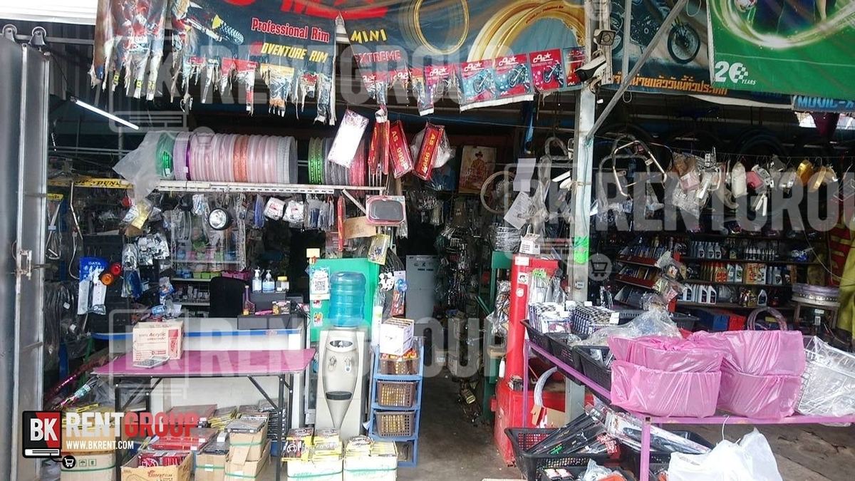 หน้าร้านอทร แขวนวงล้อ แฮนด์ และอะไหล่มอเตอร์ไซค์ ด้านหน้ามีโต๊ะสีชมพูและตะกร้าสินค้า