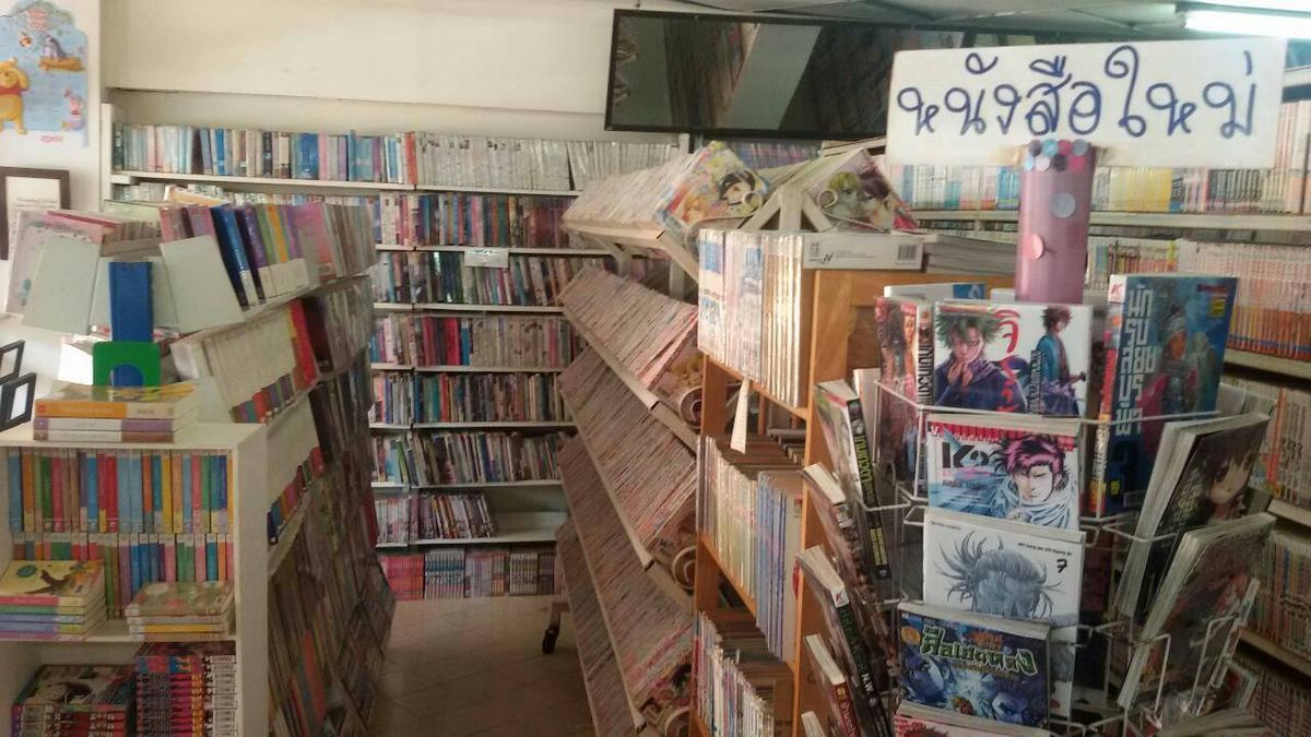 ภายในร้านปั๊กกะตืน ชั้นการ์ตูนและนิยายเรียงเต็มผนัง มีป้ายเขียนมือว่าหนังสือใหม่