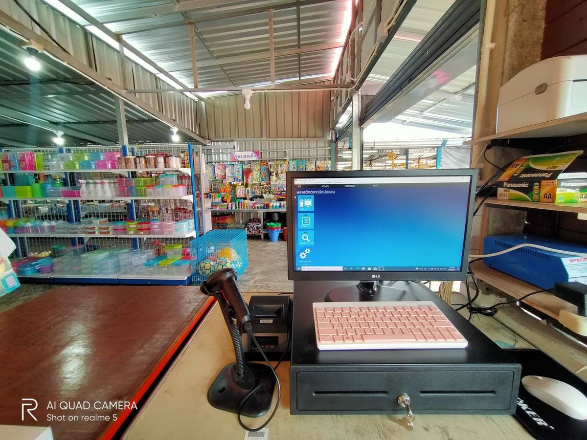จุดขายของร้านพลาสติกตลาดนัดบ่อแสน จอโปรแกรม คีย์บอร์ดสีชมพู เครื่องสแกน และชั้นเครื่องใช้พลาสติกด้านหลัง