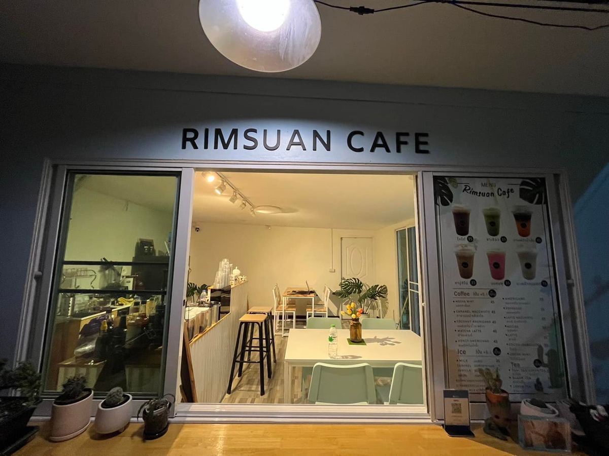 หน้าร้าน RIMSUAN CAFE ป้ายชื่อร้านเหนือประตูกระจก มองเห็นโต๊ะและเก้าอี้ภายในร้าน