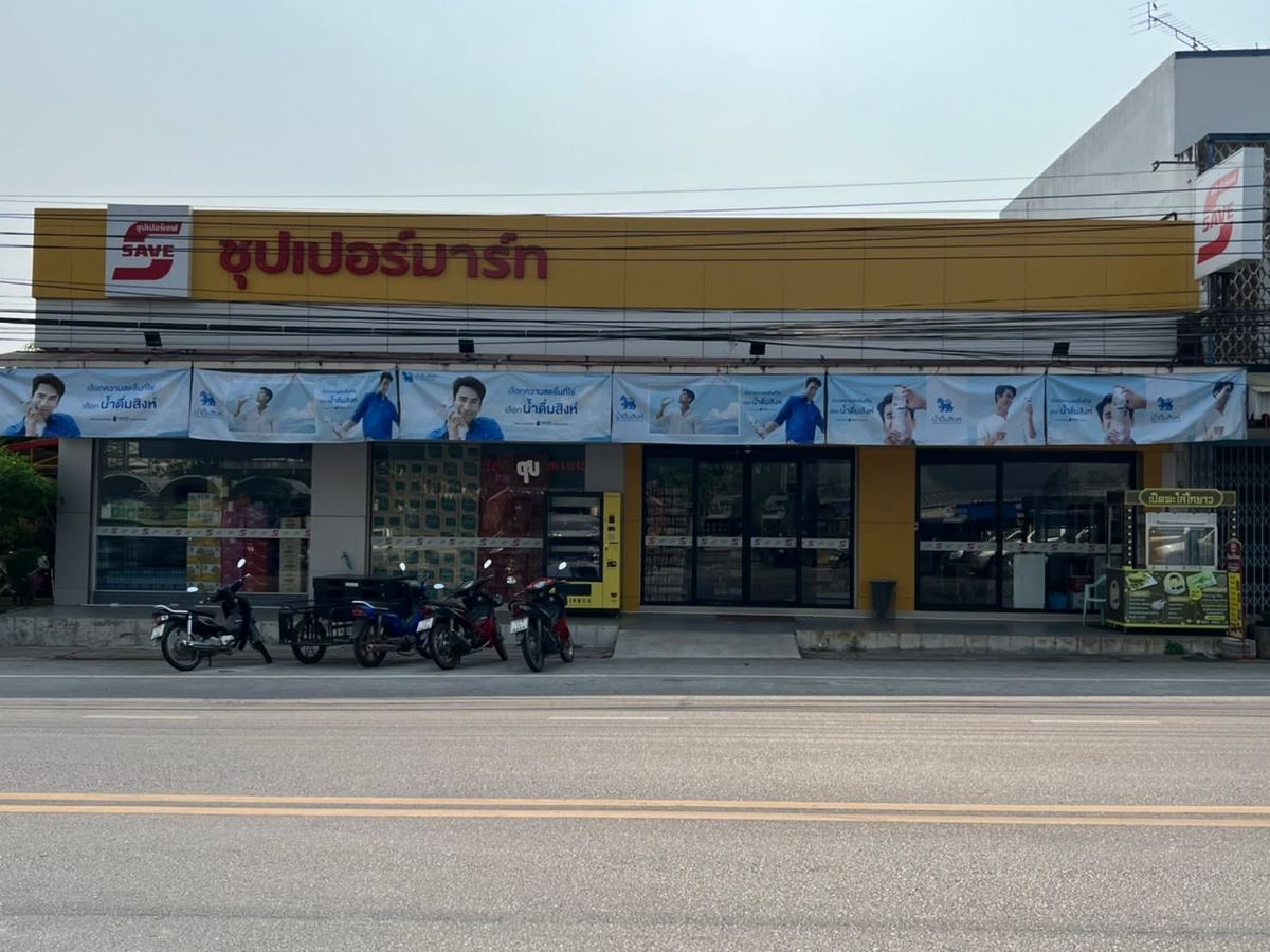 หน้าร้านซุปเปอร์เซฟ ซุปเปอร์มาร์ท ป้ายสีเหลืองยาวตลอดอาคาร มีรถจักรยานยนต์จอดหน้าร้าน
