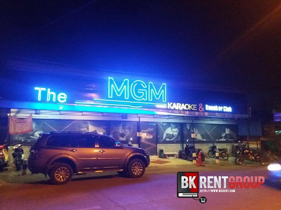 หน้าร้าน The MGM Karaoke & Snooker Club ป้ายไฟนีออนสีฟ้ายามค่ำคืน มีรถจอดหน้าร้าน