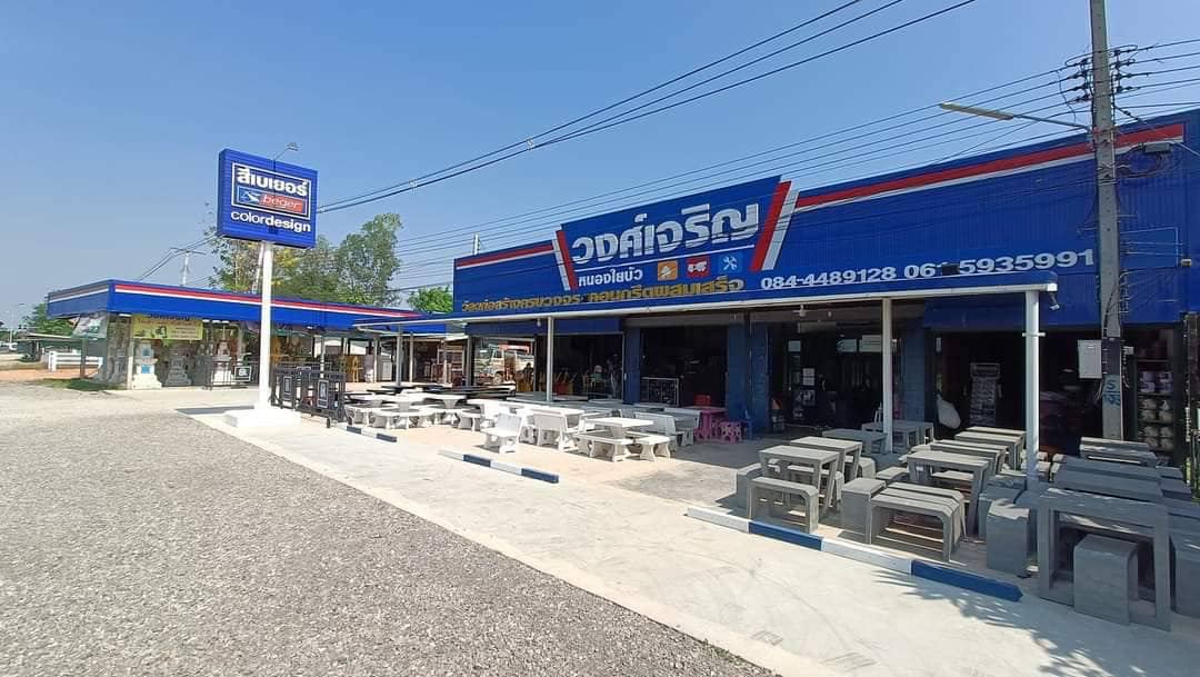 หน้าร้านวงศ์เจริญ ป้ายสีน้ำเงินยาวตลอดอาคาร ด้านหน้าวางโต๊ะและม้านั่งคอนกรีตหลายชุด